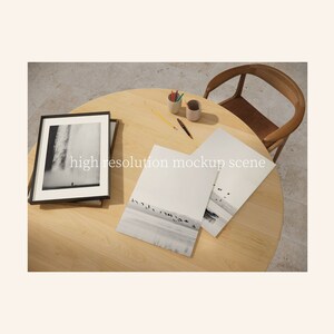 May include: A wooden table with a black framed photograph, a pencil, a cup of coloured pencils, and three sheets of paper with black and white photographs of birds flying over a body of water. The table is next to a wooden chair.