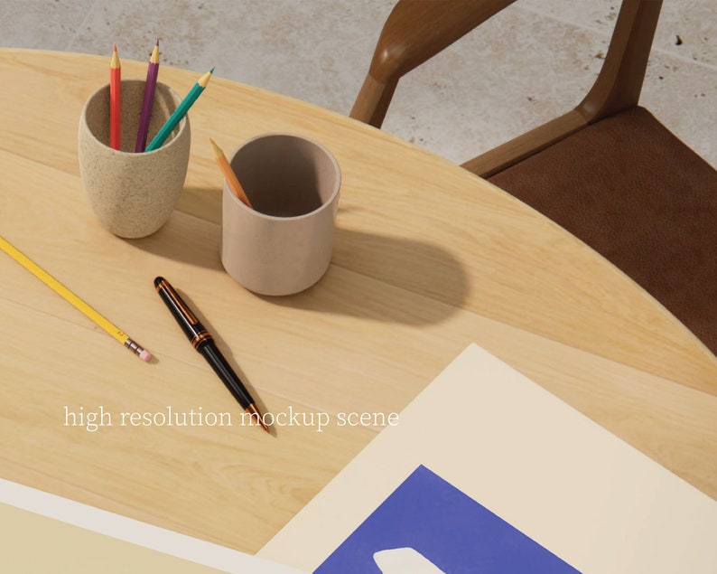 May include: A light brown wooden table with two beige pencil holders, one containing coloured pencils and the other empty. A yellow pencil and a black pen are on the table. A white sheet of paper with a blue rectangle on top is on the table. The text "high resolution mockup scene" is printed on the paper.