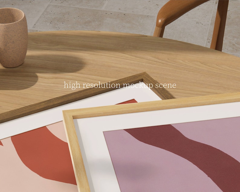 May include: Two wooden picture frames with white mats and abstract art prints in shades of pink, red, and purple. The frames are on a wooden table.