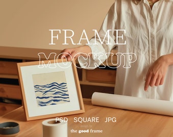 Op de afbeelding: Een houten frame mockup met een blauw en wit abstract schilderij erin. Het frame staat op een houten tafel met een witte rol papier en een zwart-witte rol tape.