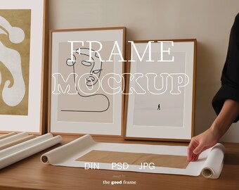 Op de afbeelding: Twee ingelijste kunstprints met een bruine houten lijst. De print aan de linkerkant toont een lijntekening van een gezicht. De print aan de rechterkant toont een minimalistisch landschap met een klein figuurtje dat in de verte loopt. De tekst "FRAME MOCKUP" is over de afbeelding gelegd. Een opgerolde canvasprint ligt op een houten tafel.
