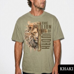 K&ouml;nnte beinhalten: Khaki-farbenes T-Shirt mit einer detaillierten Illustration eines L&ouml;wengesichts und eines Kreuzes. Der Text "THE LION OF JUDAH" ist auf das T-Shirt gedruckt. Das Shirt besteht aus einem weichen Material und hat kurze &Auml;rmel.