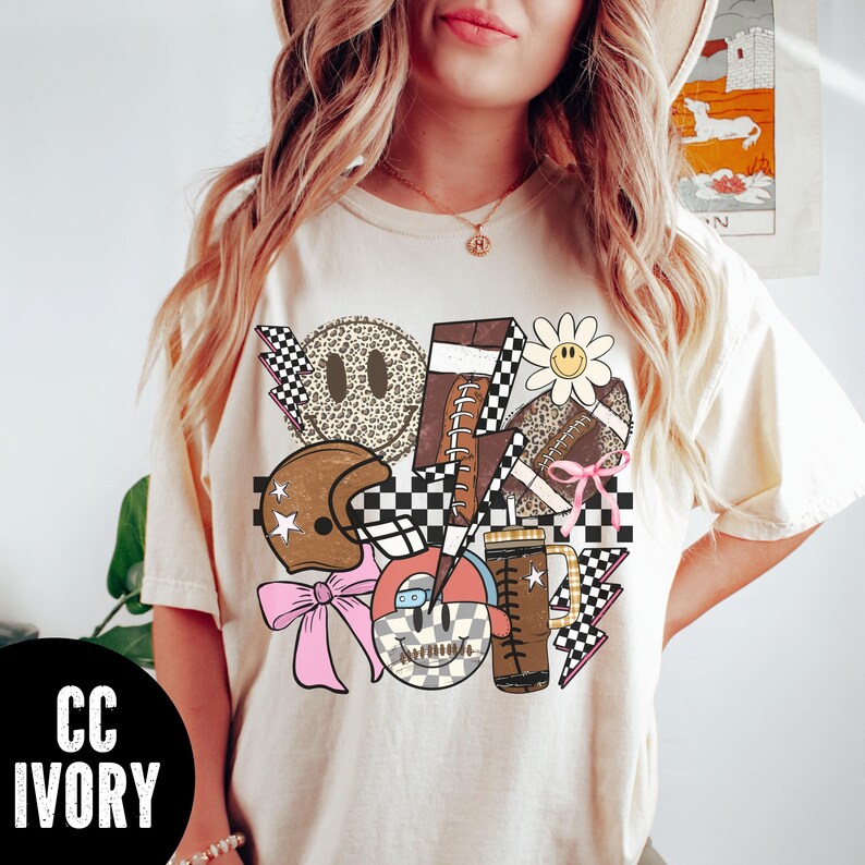 K&ouml;nnte beinhalten: Elfenbeinfarbenes T-Shirt mit einer Collage von Retro-Grafiken. Das Design umfasst einen Football, Smiley-Gesichter, einen Footballhelm, eine G&auml;nsebl&uuml;mchen und einen Bierkrug. Die Grafiken beinhalten Schachbrettmuster, Blitze und eine rosa Schleife. Der Text "CC IVORY" befindet sich in einem schwarzen Kreis.