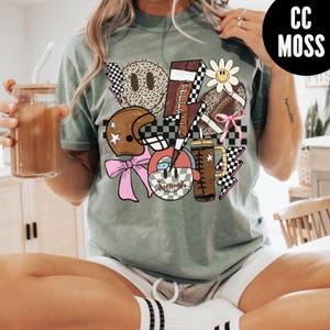 K&ouml;nnte beinhalten: Salbeigr&uuml;nes T-Shirt mit einem Grafikdesign zum Thema Football. Das Design umfasst einen Helm, Fu&szlig;b&auml;lle, Blitze, eine G&auml;nsebl&uuml;mchen und Smiley-Gesichter. Das Shirt hat eine lockere Passform und kurze &Auml;rmel.