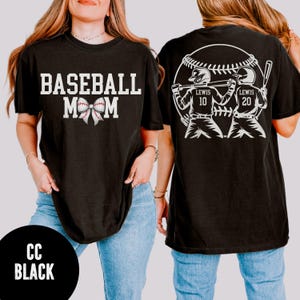 May include: Black t-shirt with the text "BASEBALL MOM" in white block letters and a bow graphic. The back of the shirt features a baseball graphic with two baseball players and the name "LEWIS" with the numbers 10 and 20. The bottom left corner of the shirt has the text "CC BLACK".