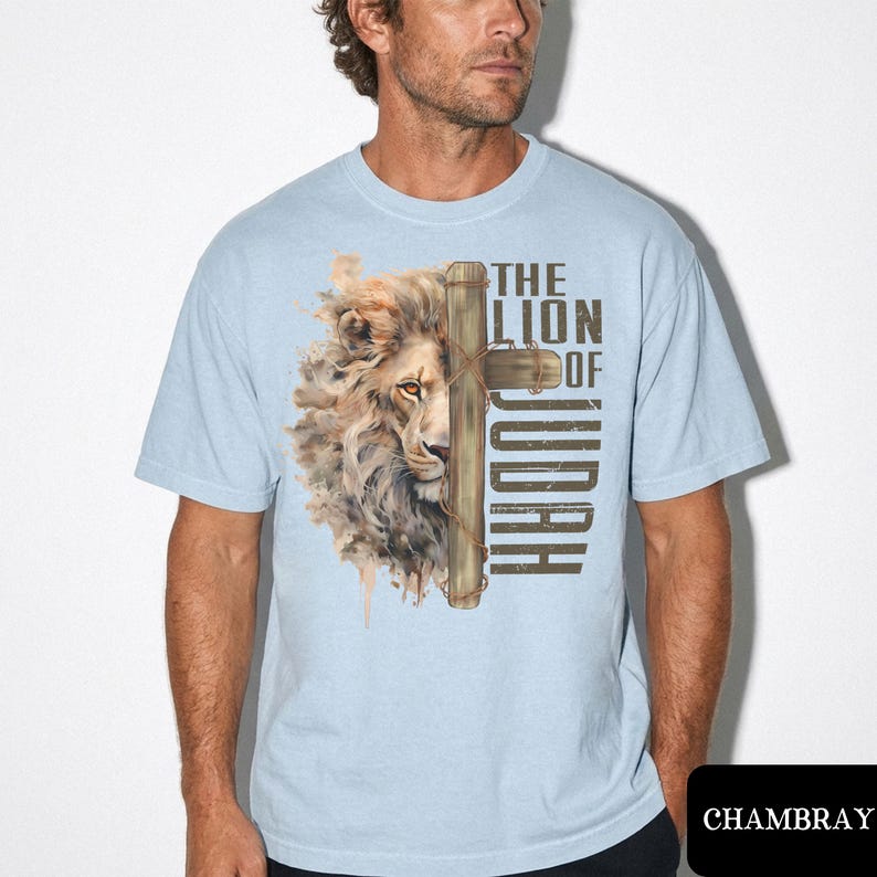 K&ouml;nnte beinhalten: Hellblaues T-Shirt mit einem L&ouml;wenkopf-Motiv und einem Kreuz. Der Text "THE LION OF JUDAH" ist vertikal aufgedruckt. Das T-Shirt besteht aus einem weichen Material. Das Design hat ein religi&ouml;ses Thema.
