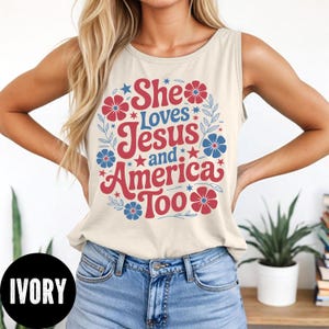 May include: Ivory tank top with the text "She Loves Jesus and America Too" in red and blue. The text is surrounded by floral and star graphics. The tank top is sleeveless and made of a soft material.