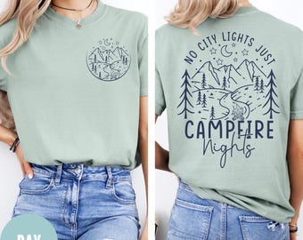 May include: A light green t-shirt with a mountain and river graphic on the front and back. The back of the shirt has the text "NO CITY LIGHTS JUST CAMPFIRE Nights". The front graphic is a smaller version of the back graphic.