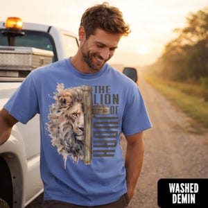 K&ouml;nnte beinhalten: Hellblaues T-Shirt mit L&ouml;wen- und Kreuz-Design und dem Text "THE LION OF JUDAH". Das Shirt ist mit "WASHED DEMIN" in einem schwarzen Rechteck gekennzeichnet. Das Shirt wird von einer Person getragen.