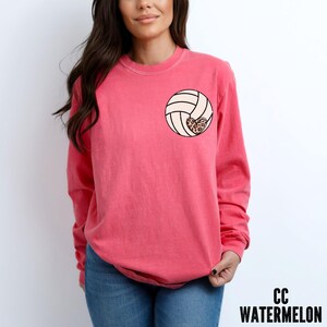 May include: A pink long-sleeved t-shirt with a volleyball graphic featuring a leopard print heart. The shirt is made of a soft, comfortable material.