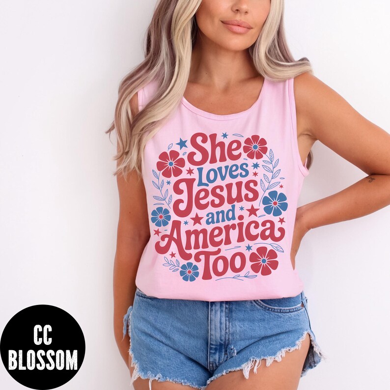 May include: A light pink tank top with the text "She Loves Jesus and America Too" in red and blue. The text is surrounded by floral and star designs. The tank top is sleeveless.