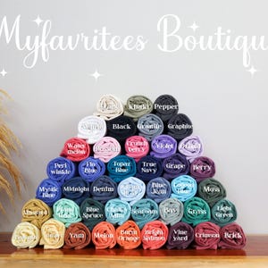 May include: A pyramid of rolled t-shirts in various colors, including black, blue, green, and pink. Each shirt is labeled with its color name. The text "Myfavritees Boutique" is displayed at the top.