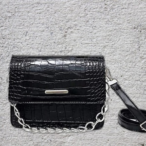 May include: A black faux leather crossbody bag with a silver chain strap and a crocodile embossed pattern.