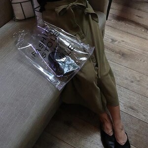 May include: A person wearing a green skirt and black shoes is holding a clear plastic bag with the text "Fashion Hole Store" printed on it.