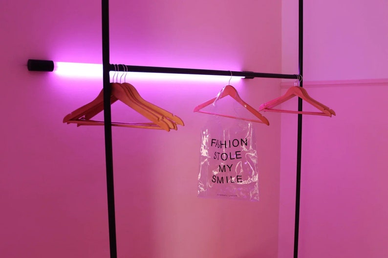 May include: Pink room with a black clothing rack and pink hangers. A clear plastic bag hangs from the rack with the text "FASHION STOLE MY SMILE".