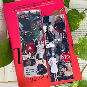 May include: A hardcover book with a bright pink cover featuring a collage of images and the title "T" in large black letters. The book has a quote and author's name at the top. A bookmark with text and images is inserted.