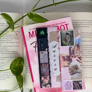 May include: Two rectangular bookmarks featuring collage designs. One bookmark displays a vertical film strip with floral and garment imagery and the name Aurora in script. The other features a montage of a person in a cloak, a castle, and hair.