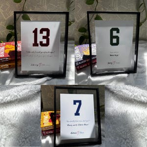 Puede incluir: Tres impresiones enmarcadas con marcos negros y fondos blancos. Cada impresión presenta un número grande en una fuente de camiseta deportiva, con una cita y nombres debajo. Los números son 13, 6 y 7. Las citas son "Creo que te necesito para siempre", "Buenas piernas", y "Literalmente escuchas a nuestro papá, ¿sabes? Cada palabra, Claire-Bear".