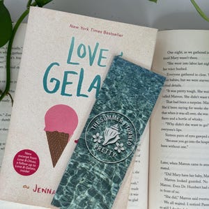Peut inclure: Un livre intitul&eacute; "Love & Gelato" avec une illustration de cornet de glace rose et un marque-page. Le marque-page pr&eacute;sente un motif de surface d'eau et le texte "The Summer I Turned Pretty".