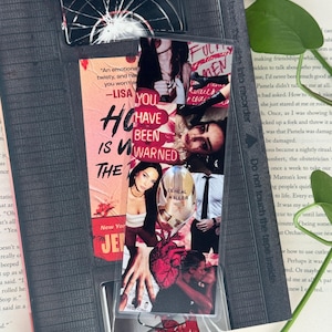 May include: A bookmark featuring a collage of images and text, including the phrases "YOU HAVE BEEN WARNED" and "CEREAL KILLER." The bookmark is inserted into a book, with a clear plastic overlay and a cracked glass design at the top.