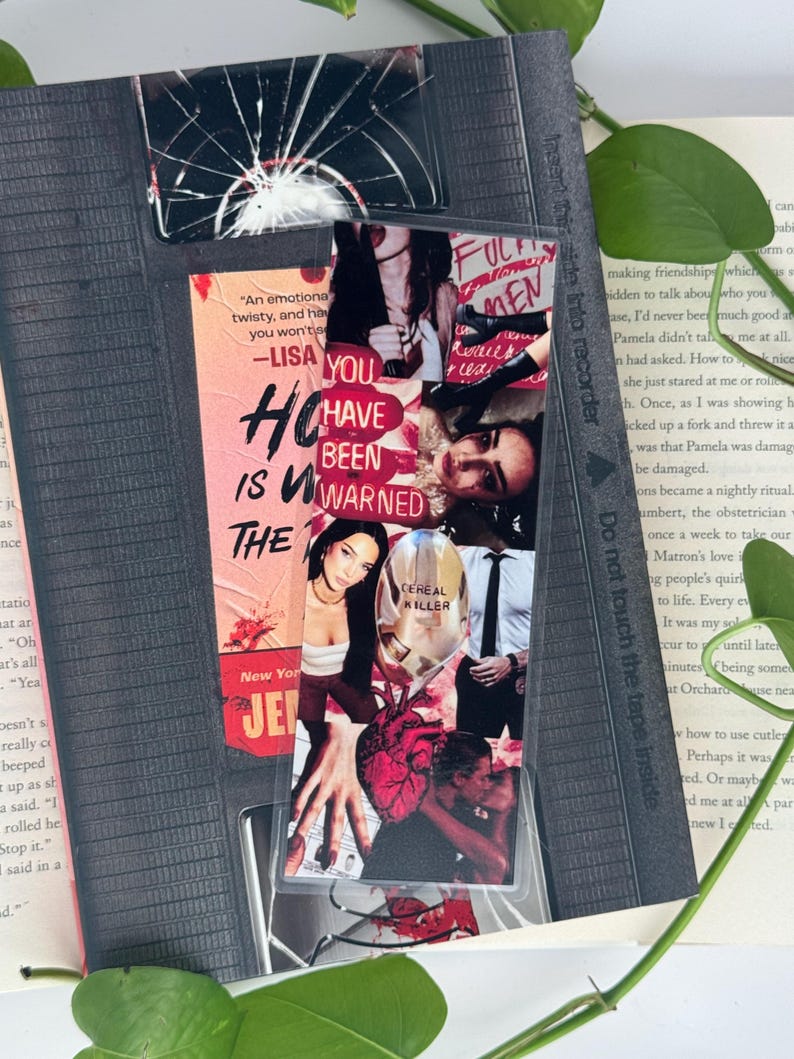 May include: A bookmark featuring a collage of images and text, including the phrases "YOU HAVE BEEN WARNED" and "CEREAL KILLER." The bookmark is inserted into a book, with a clear plastic overlay and a cracked glass design at the top.