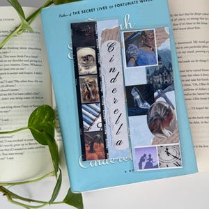 May include: A rectangular bookmark featuring a collage of Cinderella-themed imagery, including a glass slipper, a castle, and a clock, with the word Cinderella written vertically in a script font on a torn paper strip overlay.