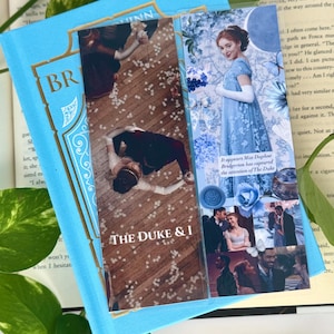 Puede incluir: Dos marcapáginas decorativos con imágenes de un drama de época, colocados sobre un libro azul claro. Uno muestra a una pareja bailando, el otro a una mujer con un vestido azul. El texto "THE DUKE & I" es visible.