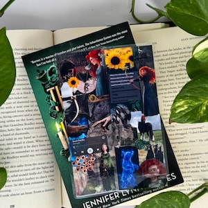 May include: A clear, rectangular bookmark featuring a collage of images, including sunflowers, a castle, and a woman with red hair. The bookmark has text that reads "JENNIFER LYNN" and "#1 New York Times bestselling author."