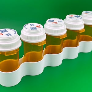 K&ouml;nnte beinhalten: F&uuml;nf durchsichtige Plastikpillenfl&auml;schchen mit wei&szlig;en Deckeln und einem roten "Walgreens"-Logo. Die Fl&auml;schchen befinden sich in einem wei&szlig;en Plastikorganizer mit f&uuml;nf F&auml;chern.