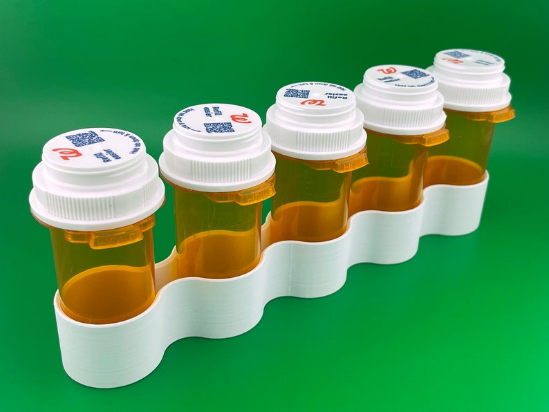K&ouml;nnte beinhalten: F&uuml;nf durchsichtige Plastikpillenfl&auml;schchen mit wei&szlig;en Deckeln und einem roten "Walgreens"-Logo. Die Fl&auml;schchen befinden sich in einem wei&szlig;en Plastikorganizer mit f&uuml;nf F&auml;chern.