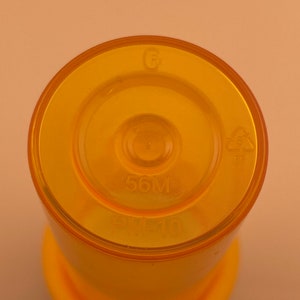 K&ouml;nnte beinhalten: Nahaufnahme der Oberseite einer gelben Plastikflasche mit einem Fassungsverm&ouml;gen von 56 ml. Die Flasche hat ein Recycling-Symbol und den Text "PM-10" aufgedruckt.