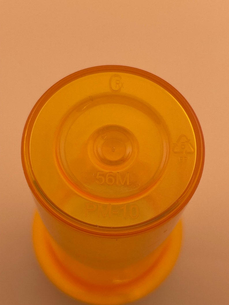K&ouml;nnte beinhalten: Nahaufnahme der Oberseite einer gelben Plastikflasche mit einem Fassungsverm&ouml;gen von 56 ml. Die Flasche hat ein Recycling-Symbol und den Text "PM-10" aufgedruckt.