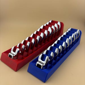 May include: Two sets of chrome wrenches in red and blue holders. The wrenches are arranged in rows, with the open ends facing up. The holders are rectangular and have individual slots for each wrench. The background is a solid tan color.
