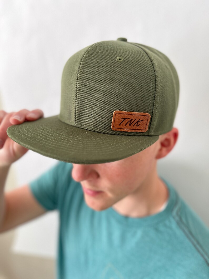 May include: A green baseball cap with a brown leather patch that says "TNK" on it.