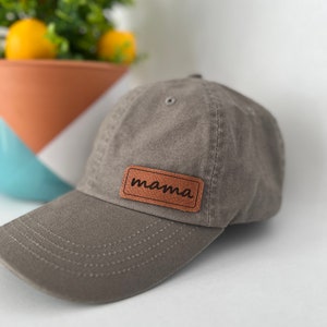 Può includere: Un cappello da baseball grigio con una toppa in pelle marrone che dice "mamma".