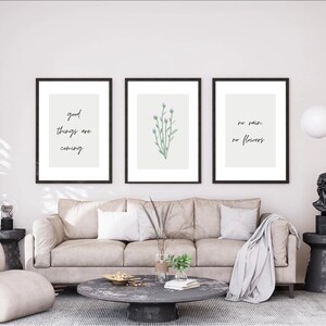 Puede incluir: Tres impresiones enmarcadas en una pared blanca sobre un sofá beige. La impresión de la izquierda tiene el texto "good things are coming". La impresión del medio presenta una ilustración de acuarela de flores moradas. La impresión de la derecha tiene el texto "no rain, no flowers".