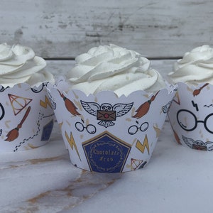 May include: Three cupcakes with white frosting in decorative paper cups. The cups feature a repeating pattern of glasses, a broom, an owl, and lightning bolts. One cup has the text "Chocolate Frog".