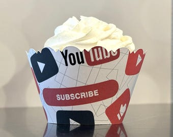 Puede incluir: Un cupcake con glaseado blanco en un envoltorio de papel decorativo. El envoltorio presenta un patrón repetido de logotipos de YouTube, botones de reproducción y la palabra "SUBSCRIBE" en rojo y blanco.
