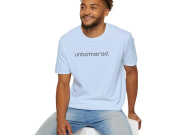 May include: A light blue t-shirt with the word "unbothered" printed in a dark blue font. The shirt is being worn by a person wearing blue jeans.