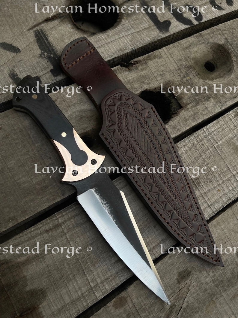Op de afbeelding: Een zwart en bruin mes met een zilveren lemmet en een leren schede. De schede heeft een decoratief patroon en de tekst "Laycan Homestead Forge" is erop gegraveerd.