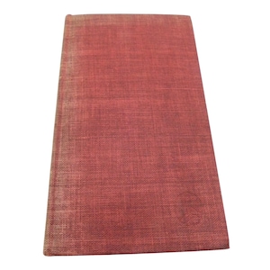 May include: A rectangular book with a textured, reddish-brown cover. The cover has a woven appearance, with visible horizontal and vertical lines. The edges of the book show slight wear and discoloration, suggesting age or use. The book is set against a white background.