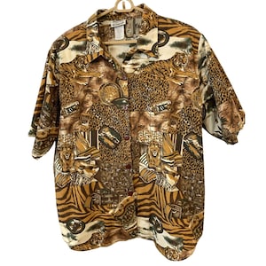 May include: A short-sleeve button-down shirt featuring a brown, tan, and black collage print of tigers, lions, and leopard spots. The shirt has a pointed collar, a front button placket with dark brown buttons, and a loose, relaxed fit silhouette.
