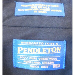 May include: A dark navy blue garment interior featuring two blue rectangular fabric labels with yellow text. The top label reads ASSEMBLED IN MEXICO OF FABRIC FROM THE U.S.A. 100% VIRGIN WOOL MACHINE WASHABLE RN 29685. The bottom label reads PENDLETON.