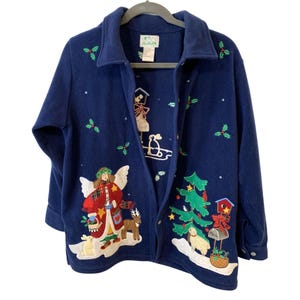 May include: A navy blue fleece jacket featuring embroidered holiday motifs including an angel, a reindeer, a Christmas tree, a mailbox, and holly leaves. The jacket has a collared neckline, long sleeves, and a button-front closure with a white label.
