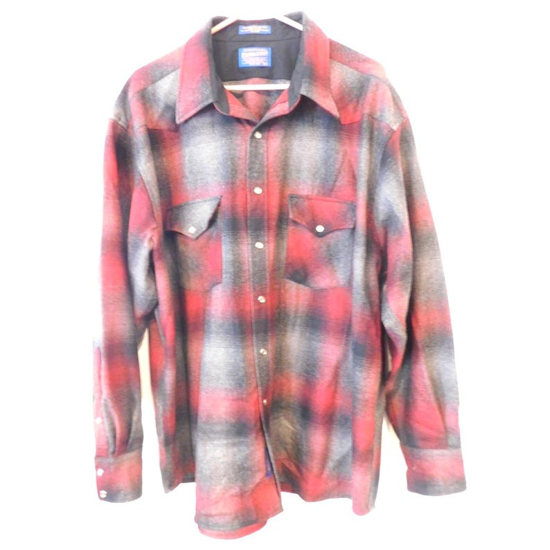 May include: A long-sleeve button-down shirt featuring a red and grey plaid pattern. The shirt includes a pointed collar, two chest pockets with button-down flaps, and a series of buttons running down the center front and on the sleeve cuffs.
