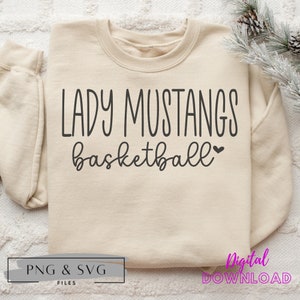 May include: A beige sweatshirt with the text "LADY MUSTANGS basketball" in black lettering. The text is in a handwritten font with a small heart symbol after the word "basketball".