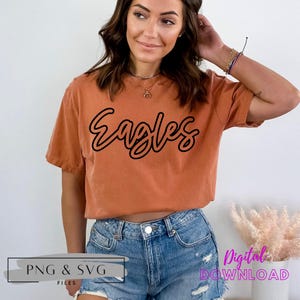 K&ouml;nnte beinhalten: Ein digitaler Download eines Grafikdesigns mit dem Wort "Eagles" in schwarzer Umrandung mit wei&szlig;er F&uuml;llung. Das Design befindet sich auf einem rostfarbenen T-Shirt.