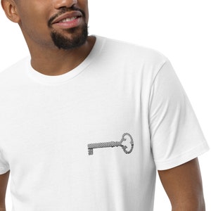May include: White t-shirt with a small, embroidered key design on the chest. The key is detailed with a textured pattern, offering a classic and understated aesthetic. The shirt is made of a soft material.