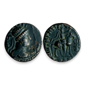 May include: Two antique bronze coins. One coin features a profile of a person wearing a head covering. The other coin depicts a scene with two figures and an animal. Both coins have a dark green patina and are set against a white background.