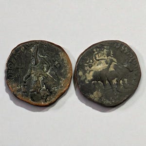 May include: Two antique bronze coins. One coin features a standing figure with a staff, the other depicts a horse and rider. Both coins show signs of wear and age, with visible details.